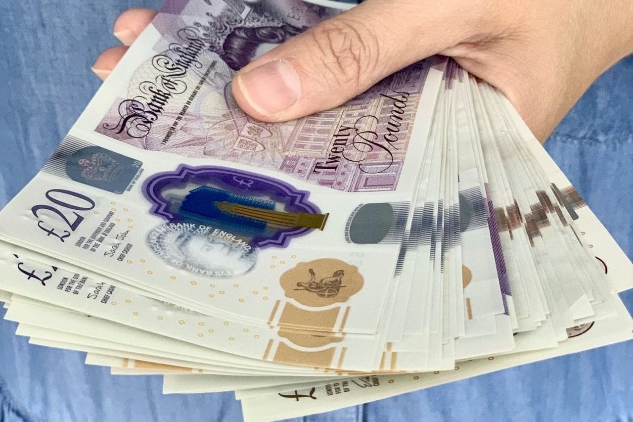 A woman in blue denim dress is holding on money. Pound sterling, cash, bank notes, savings, payment